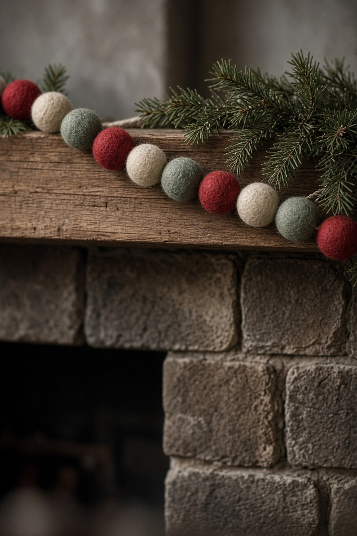 Handmade wool felt ball garland in red, cream and sage draped on a rustic wooden mantel